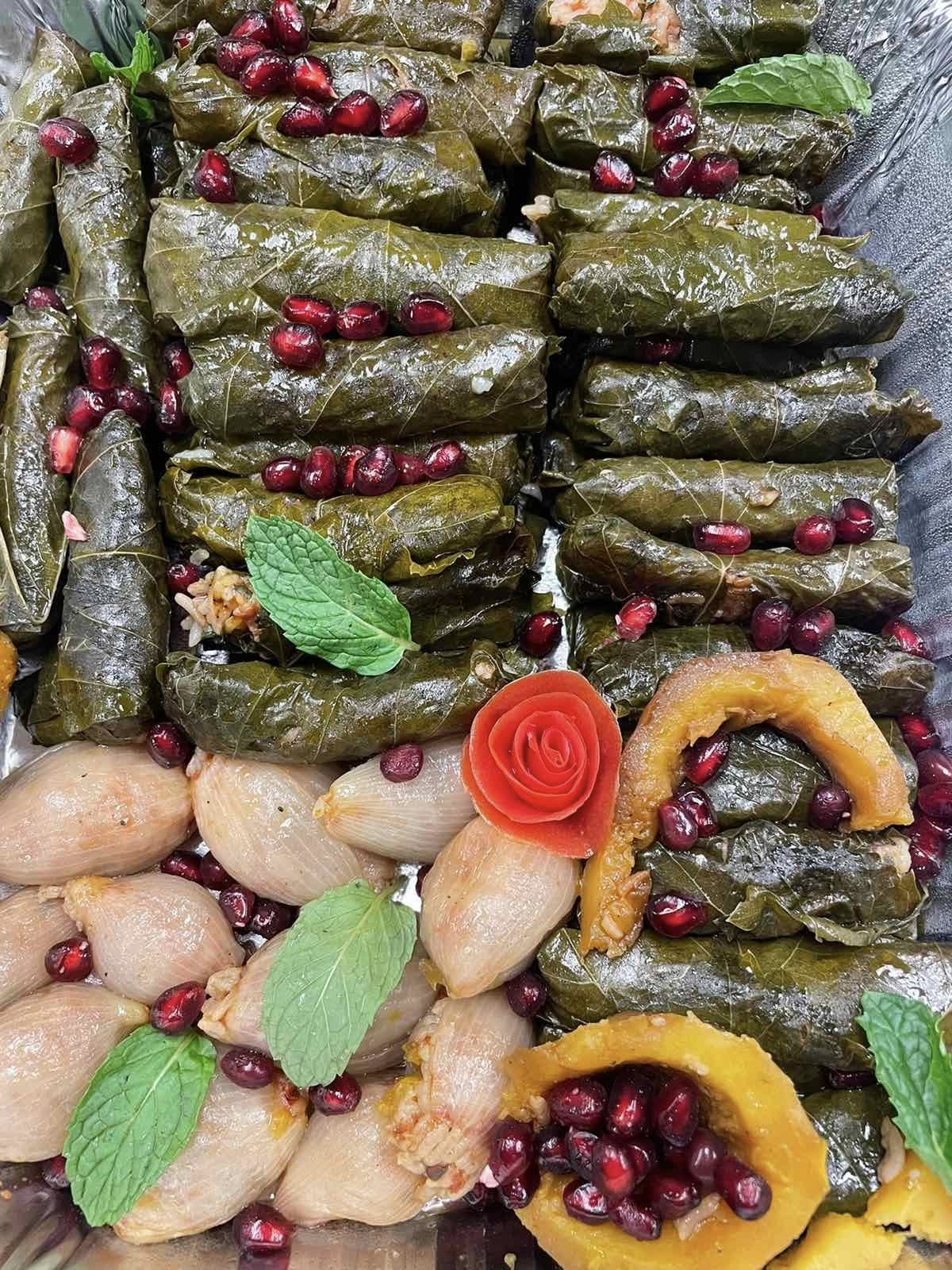 Catering tray of grape leaf dolma, stuffed onions and squash with pomegranate seeds